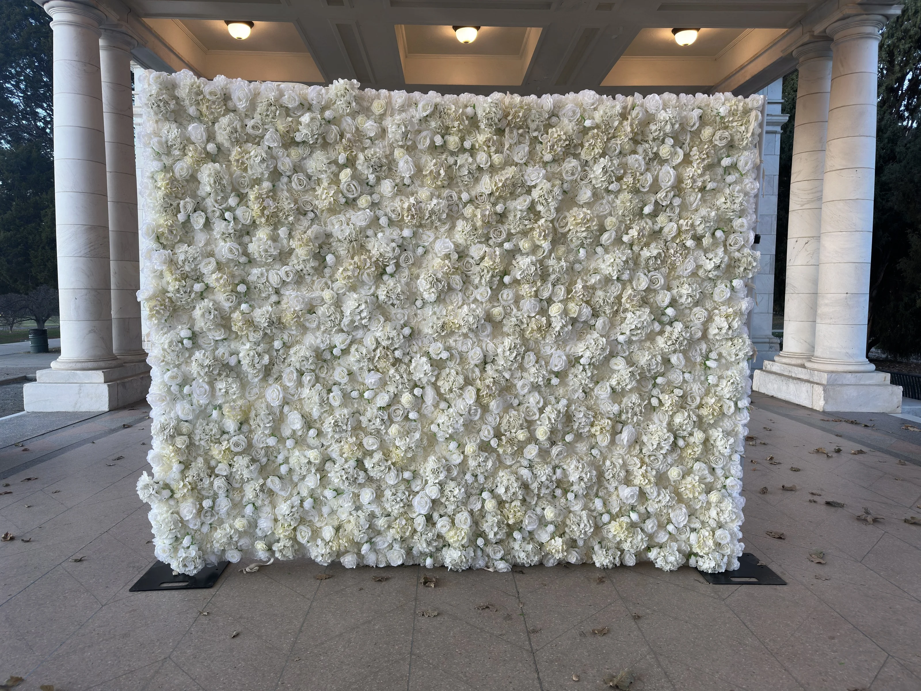 Ivory rose and hydrangea flower wall standing beneath a columned pavilion at dusk