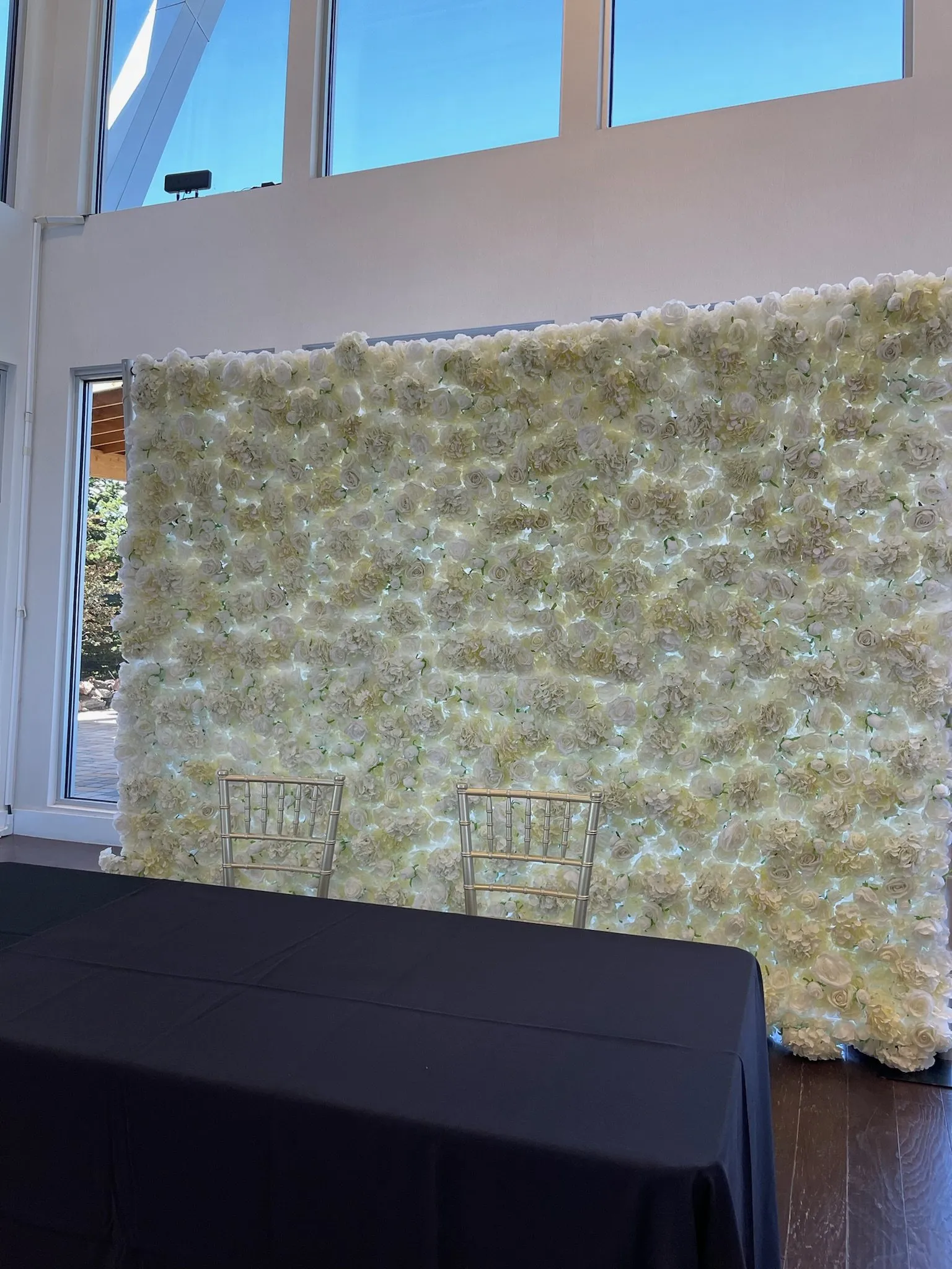 Flower wall behind a reception table by tall windows